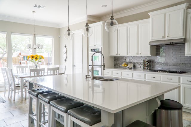 A bright, modern kitchen with a large white island, gray bar stools, and stainless steel appliances